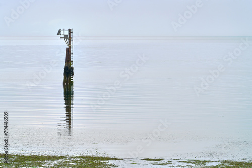 Marine Navigation Aid near Shore. A fixed Navigation Aid with an attached weather sensor marking shallow water on a misty day.