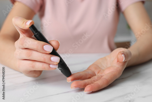 Diabetes. Woman using lancet pen at white marble table, closeup