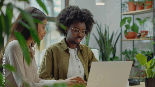 Female executive manager supervising black colleague who is working on laptop in office.