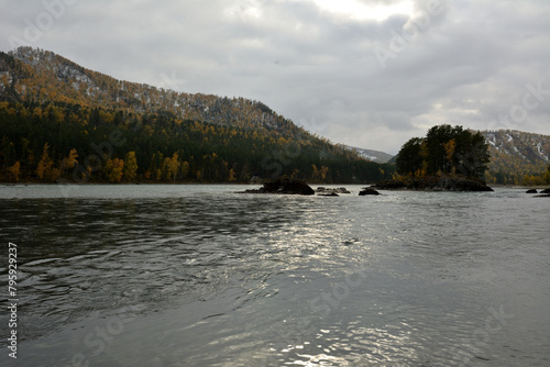 Stone ledges in the bed of a wide mountain river flowing through the autumn taiga on a cloudy day.