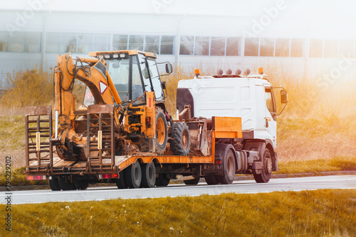 Flatbed Truck delivering heavy machinery to the construction site. Excavator tractor or crane. Construction industry.