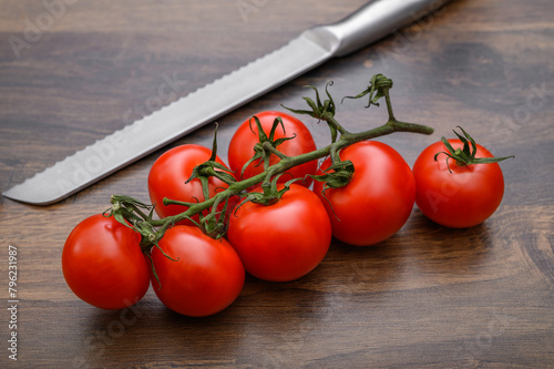 Duży stalowy nóż obok dojrzałych pięknych czerwonych pomidorów na gałązce leżą na blacie kuchennym 