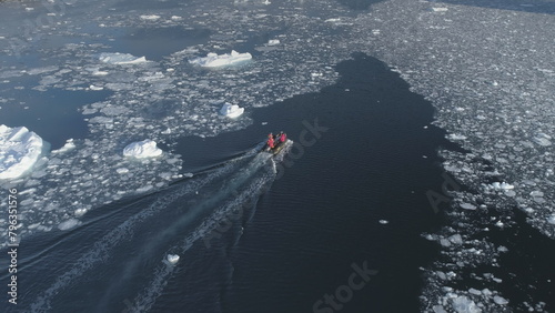 Zodiac motor boat sailing in Antarctic ice. Aerial tracking - drone flight overview of south pole ocean landscape. Rubber boat float in winter open water brash ice.
