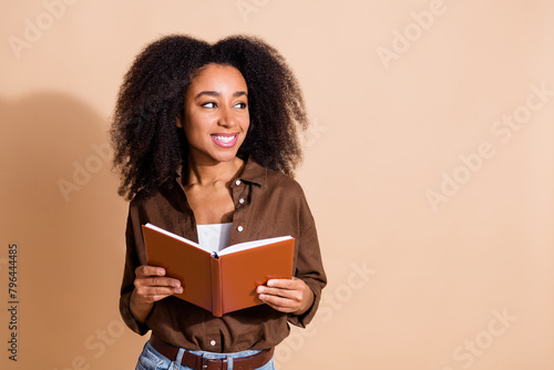 Photo of clever girl with perming coiffure wear brown blouse hold book look at offer empty space isolated on pastel color background