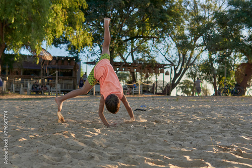 latino little boy playing on the sand doing pirouettes a sunny day on the beach..