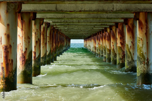 Rusty pillars of old sea pier create mesmerizing seascape scene with view from under pier, restless sea waves crashing on rock symbolizing harmonious yet powerful coastal symphony