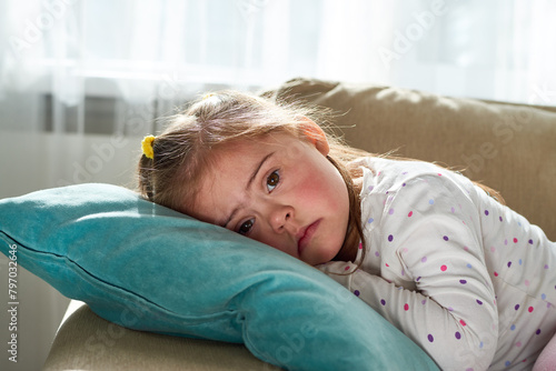 Portrait of cute little girl with Down syndrome looking at camera lying down on pillow