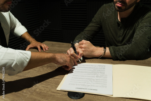 Close-up of a suspect signing an immunity deal in the shadows during an interrogation