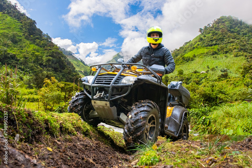 Man on quad bike. Motorcyclist in green mountains. Man ATV driver in yellow helmet. All-terrain motorcycle for off-road driving. Guy drives ATV. ATV driver looks ahead. Quad bike race