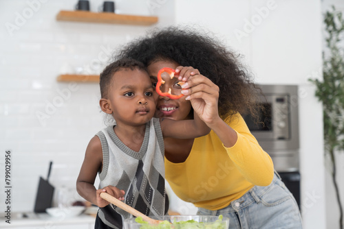 African American young mother cooking with little son in kitchen room at home