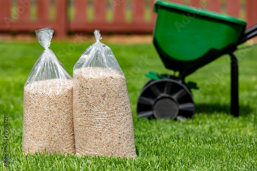 Bags of lawn fertilizer and herbicide with broadcast spreader in yard with healthy grass. Lawn care, weed control and landscaping concept.
