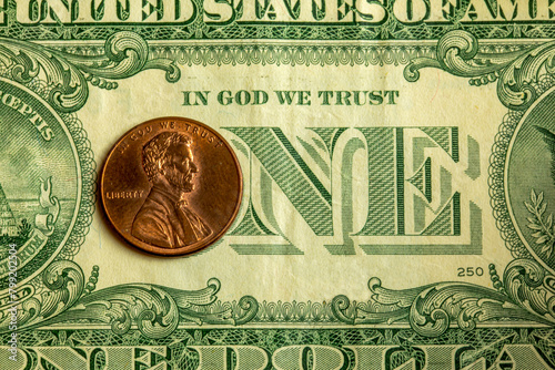 Detail of a one dollar bill with a Abraham Lincoln coin over the "o" in "one" and the phrase "in God we trust"