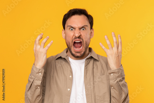 Frustrated Man Expressing Anger With Raised Hands Against Yellow Background