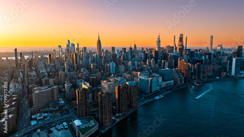 Orange light of setting sun illuminating the skyscrapers and high-rise buildings in New York scenery. Top view on the metropolis from above the East River.