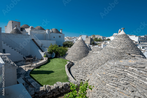 Beautiful stone of Trulli houses with white walls, narrow streets, decorated with flowers, palm trees and other decorations. Spring day, warm with sun and blue skies Selling souvenirs