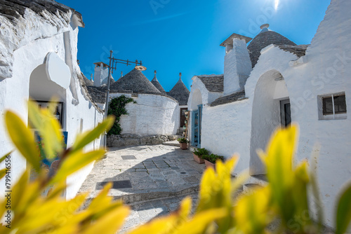 Beautiful stone of Trulli houses with white walls, narrow streets, decorated with flowers, palm trees and other decorations. Spring day, warm with sun and blue skies Selling souvenirs