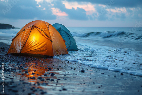 A pair of colorful tents pitched on a sandy beach, with waves gently lapping at the shore in the background.
