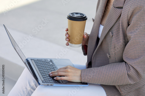 Successful businesswoman multitasks, savouring a hot beverage and working on her laptop in a serene outdoor setting