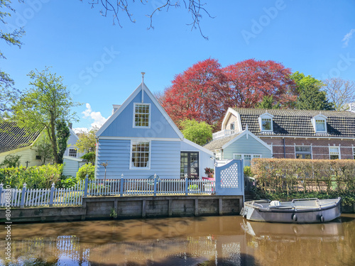 A quaint blue house peacefully sits beside a calm body of water, surrounded by a tranquil and picturesque setting