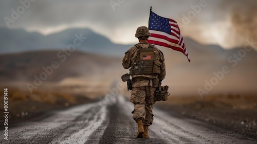 A soldier proudly walks down the asphalt road, holding the American flag as a symbol of his service in the army. The vehicles tires hum on the pavement under the vast sky