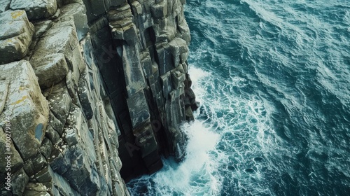 The aerial view shows the vast expanse of the ocean with towering cliffs along the coastline. Waves crash against the rocky formations creating a dynamic and rugged landscape.