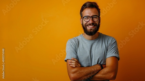 A Young handsome man with beard wearing casual t-shirt and glasses over yellow background happy face smiling with crossed arms looking at the camera, Positive person