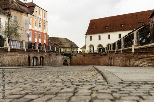 A narrow cobbled street is lined with colorful buildings with red tiled roofs and decorative facades, wrought iron balconies and window grills on some of the buildings add to the old world charm.