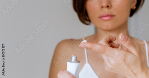 A woman presses the ointment onto her finger and applies it to the bite site by a bedbug on her shoulder on a white background, close-up. Skin health problem. Red pimples.