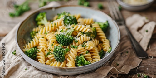 A serene setting with a bowl of fusilli pasta topped with steamed broccoli, accompanied by a beige linen napkin and a modern fork on a wooden surface