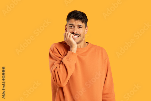 Man in Orange Sweater Holding Hand to Face