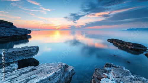 Tranquil and serene, this image captures the soft glow of sunset with perfect reflections on the sea's smooth surface beside rugged cliffs
