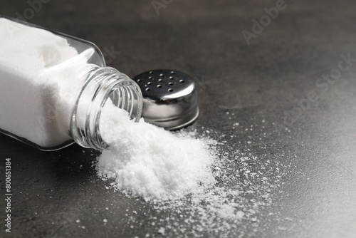 Overturned shaker with salt on grey table, closeup. Space for text