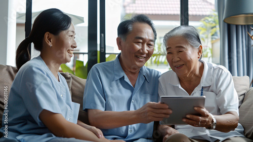 an asian nurse holds one and shows it to the elderly couple sitting on the couch in the living room