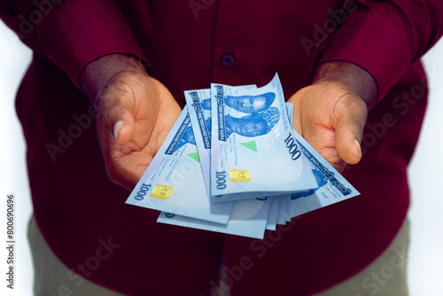 Black man in red long sleeve shirt having holding 1000 Nigerian Naira notes in opened palms