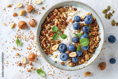 Homemade organic buckwheat granola with yogurt blueberries hazelnuts peanuts nutmeg pumpkin seeds and flax seeds in a ceramic bowl Healthy breakfast on light back