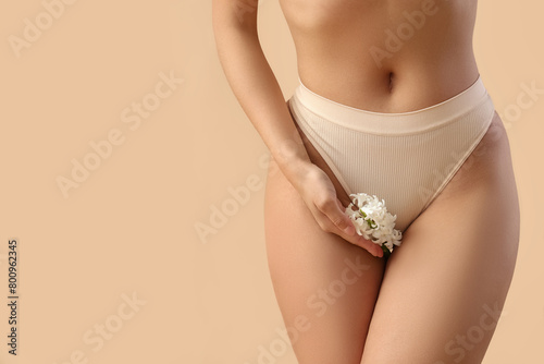 Beautiful young woman in panties with hyacinth flowers on beige background, closeup