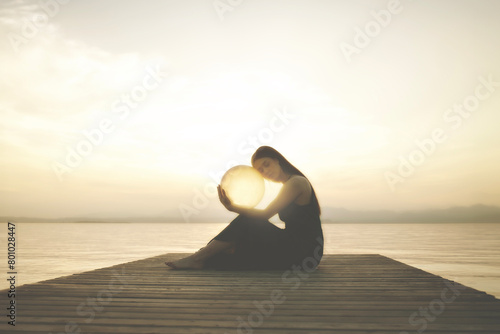 woman hugging a surreal sphere illuminated by the sun that releases energy, abstract concept