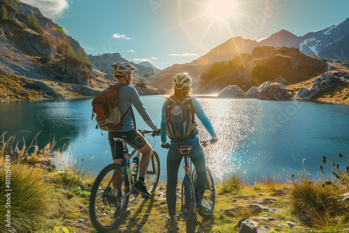 Young couple mountain biking looking at a bright blue mountain lake. The lake could be in the Alps, for example in Austria or Switzerland (A.I.-generated)