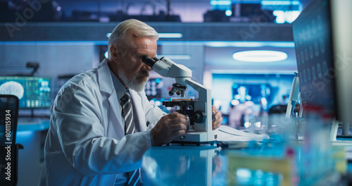 Medical Development Laboratory: Senior Caucasian Male Scientist Using Microscope, Analyzes Petri Dish Sample. Big Pharmaceutical Lab Conducting Biotechnology Research, Developing Innovative Drugs.