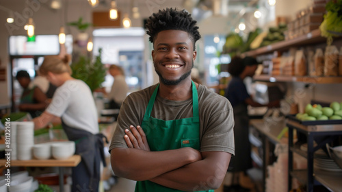 A cheerful young man in a green apron, arms crossed, oversees his eco-friendly store bustling with activity.