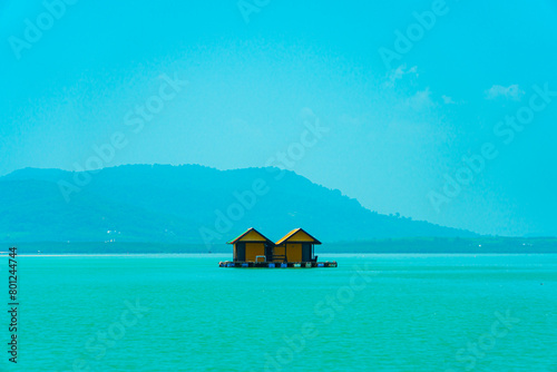 Small floating houses between the horizon line that separates the sea from the sky and set against a backdrop of plains and mountains. Floating houses used by fishermen as a place to cultivate fish