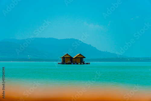 Small floating houses between the horizon line that separates the sea from the sky and set against a backdrop of plains and mountains. Floating houses used by fishermen as a place to cultivate fish
