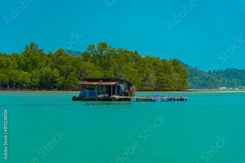 Small floating houses between the horizon line that separates the sea from the sky and set against a backdrop of plains and mountains. Floating houses used by fishermen as a place to cultivate fish