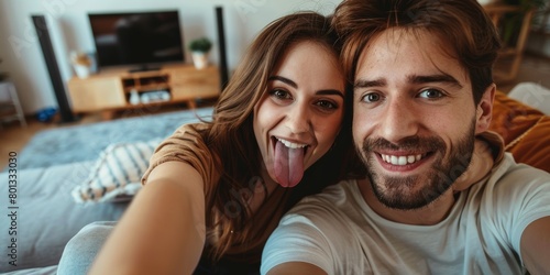 Funny romantic couple pulling faces and fooling around while holding a mobile phone and taking a selfie together. Fun couple taking a picture or video call.