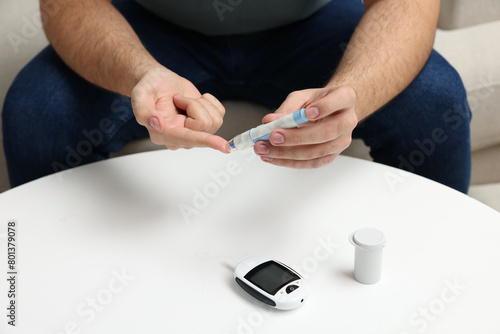 Diabetes test. Man checking blood sugar level with lancet pen at white table, closeup