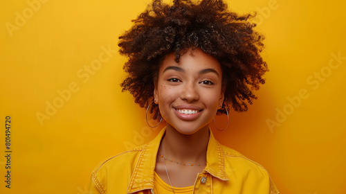 Young african american girl with afro hairstyle smiling and looking at camera isolated over yellow background