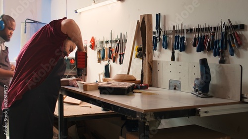 Woodworker in assembly shop using power drill to create holes for dowels in wooden board. Carpenter sinking screws into wooden surfaces with electric tool, doing precise drilling for seamless joinery