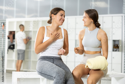 Two young athletic women talking in locker room after training