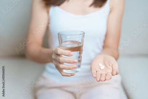 woman hand holding medicine painkiller pill and water glass on the sofa at home, taking for headaches, stomach ache, Diarrhea Pain from food poisoning, Endometriosis, Hysterectomy and Menstrual