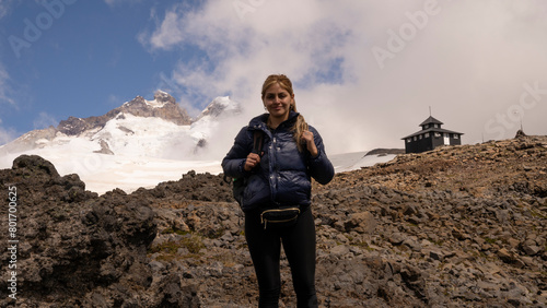 Outdoor activities. Extreme sports. Portrait of a woman hiking high in the Andes cordillera. The Tronador hill peak and Otto Meiling wooden refuge in the background